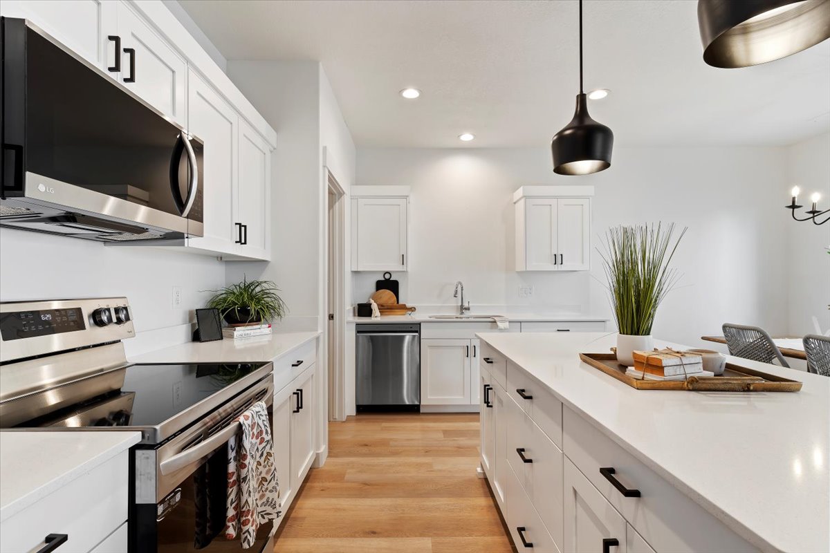 Modern kitchen featuring white shaker cabinetry, stainless steel appliances, a large center island with a white countertop, and light wood-finish flooring