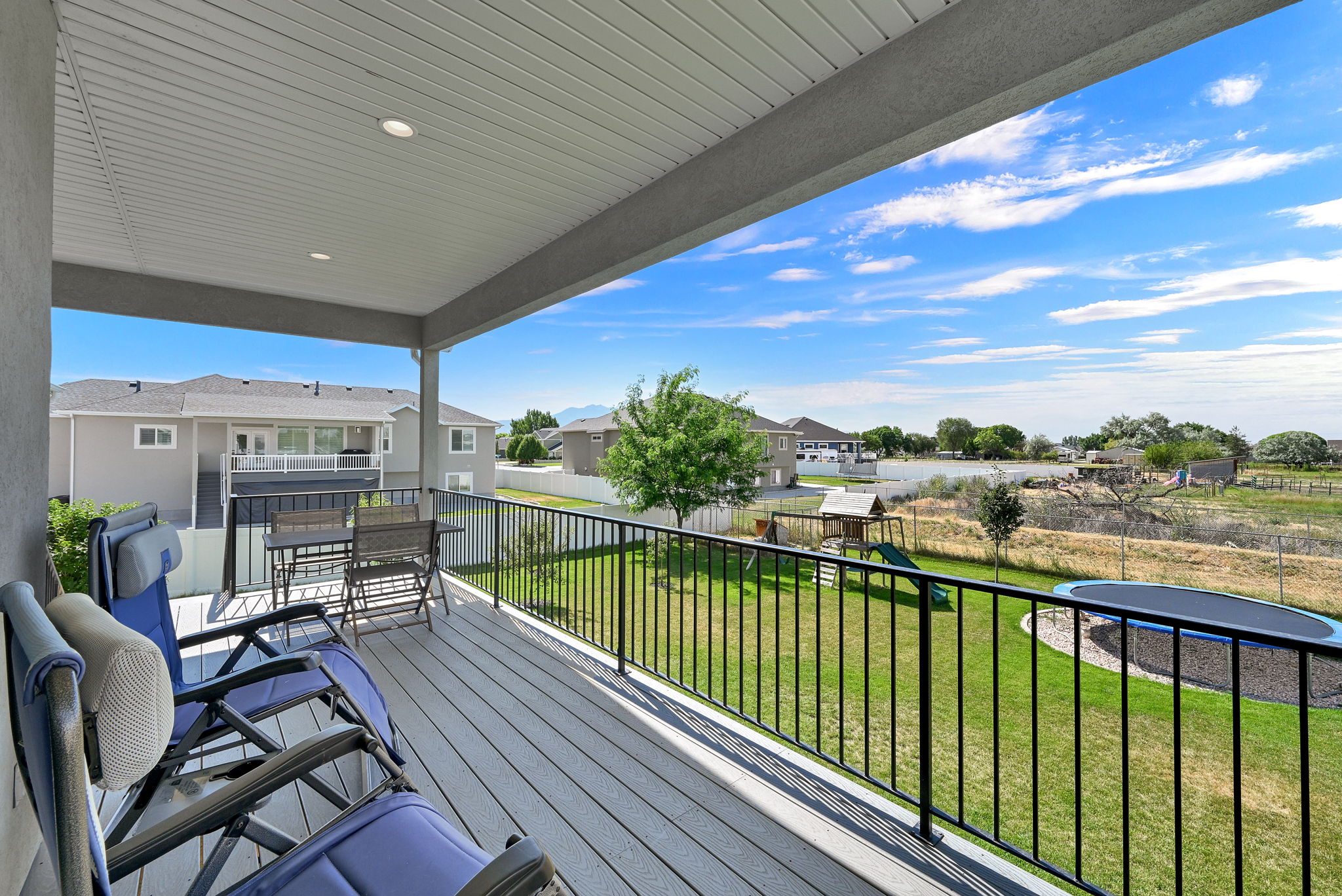 Covered outdoor deck with light gray wood-finish flooring, recessed lighting, and black metal railings