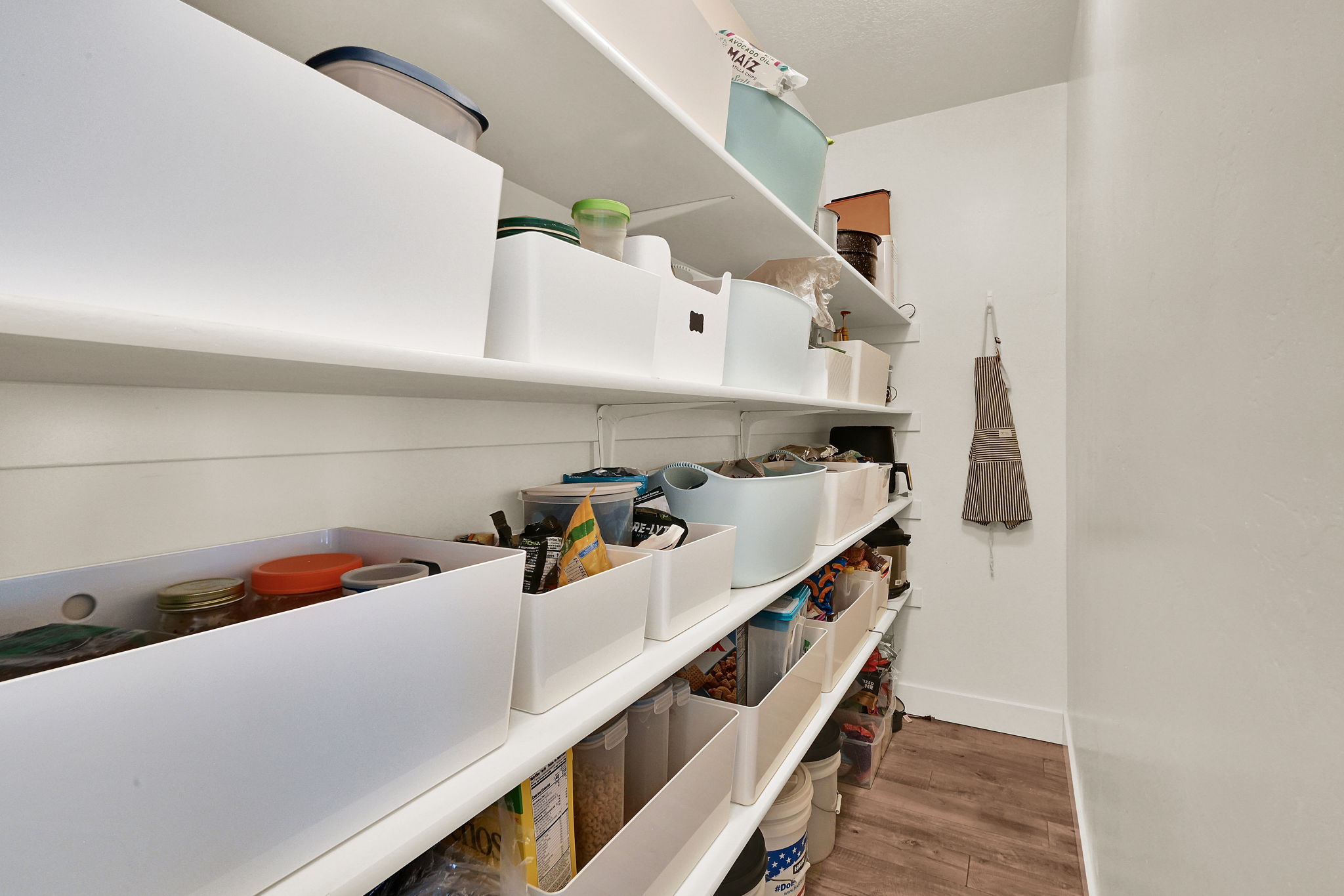 Pantry featuring built-in shelving, white walls, and wood-finish flooring
