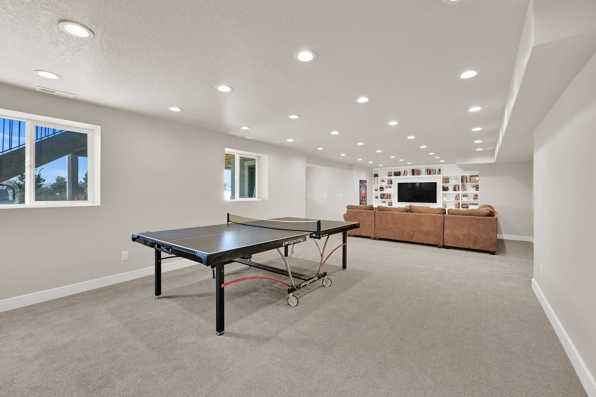 Spacious recreation area featuring light gray carpeting and multiple recessed ceiling lights