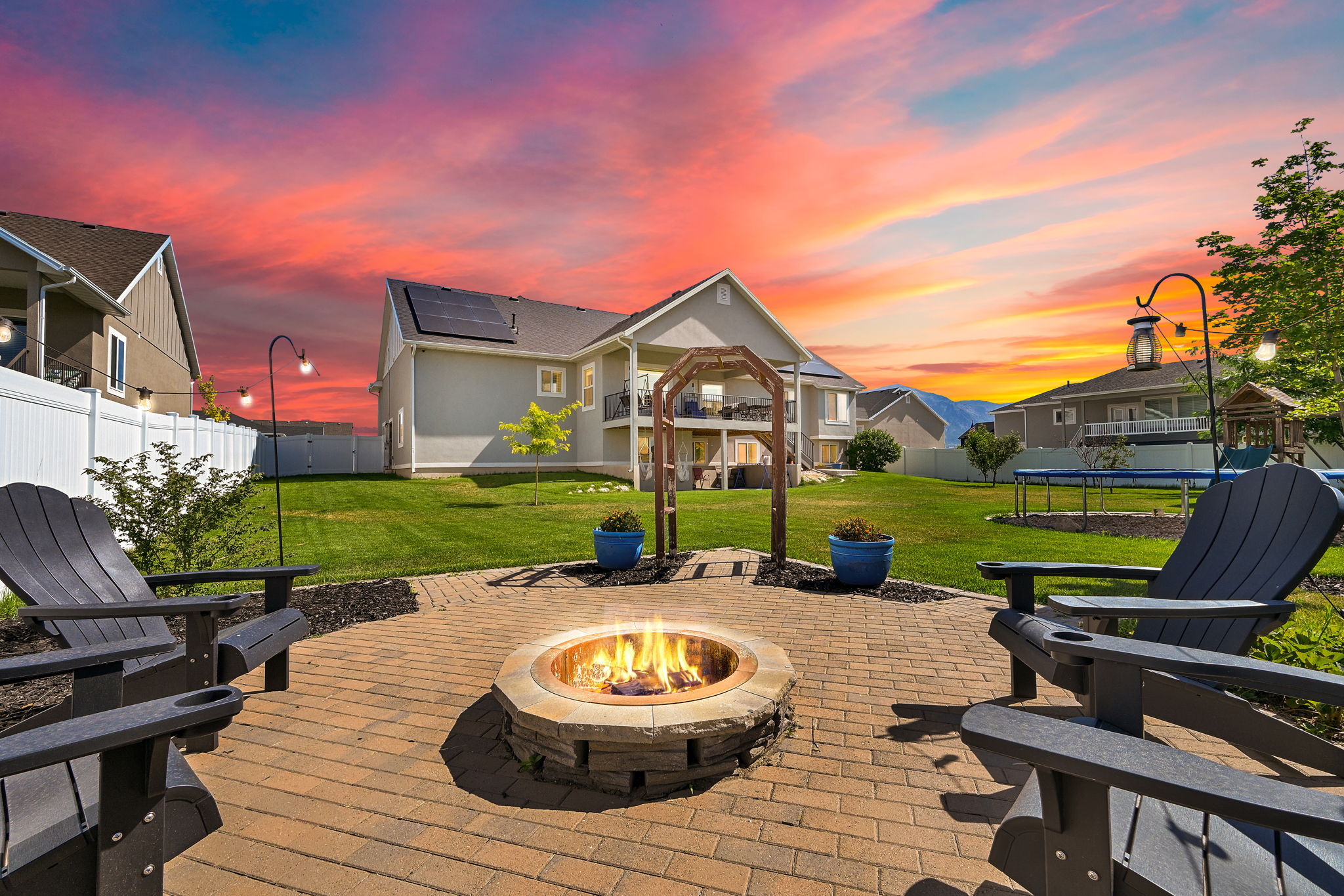 Expansive backyard featuring a paver patio with a built-in fire pit, a sprawling lawn, and a white privacy fence