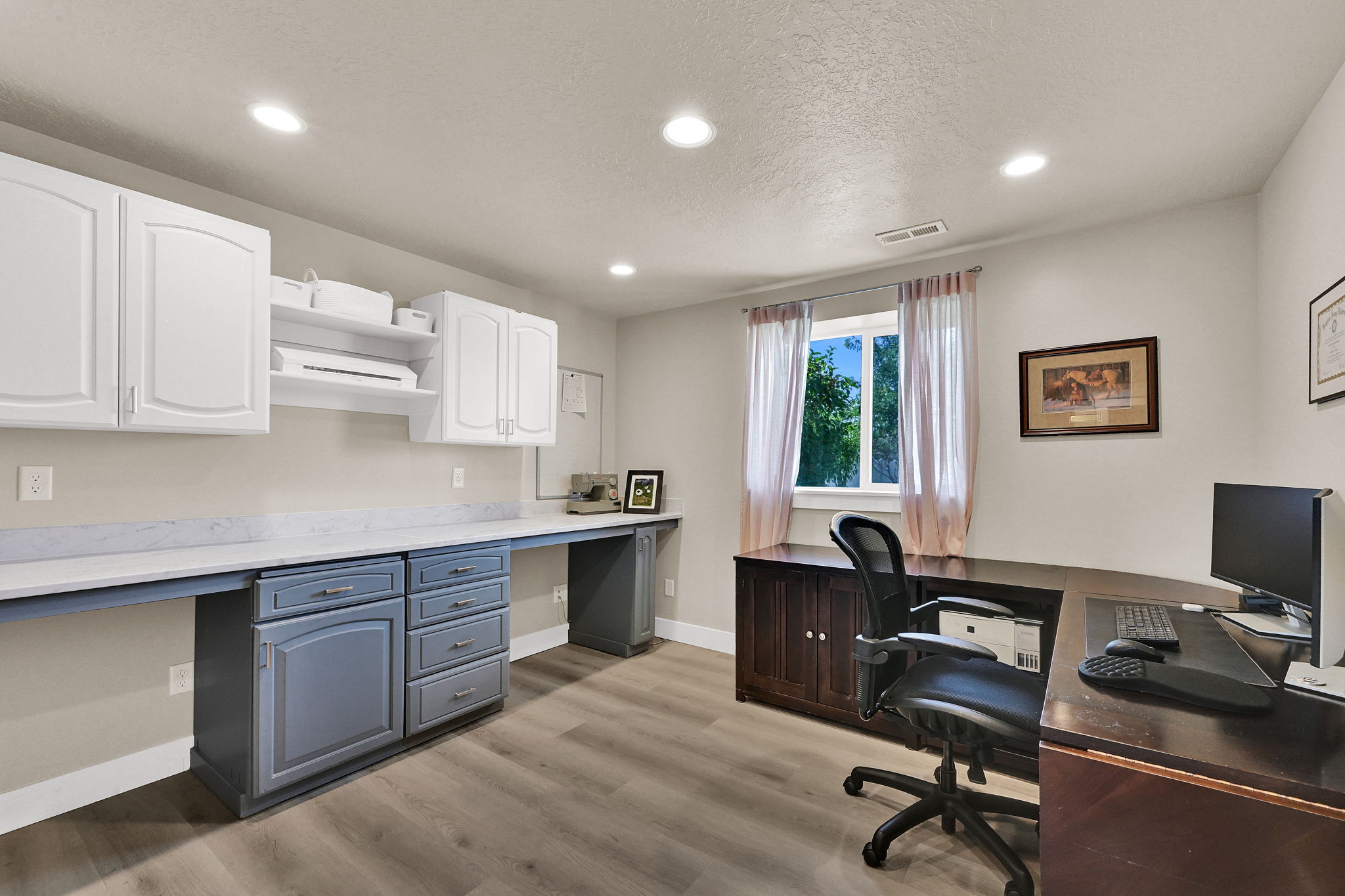 Dedicated workspace featuring extensive built-in cabinetry, wood-finish flooring, recessed lighting, and a window with natural light