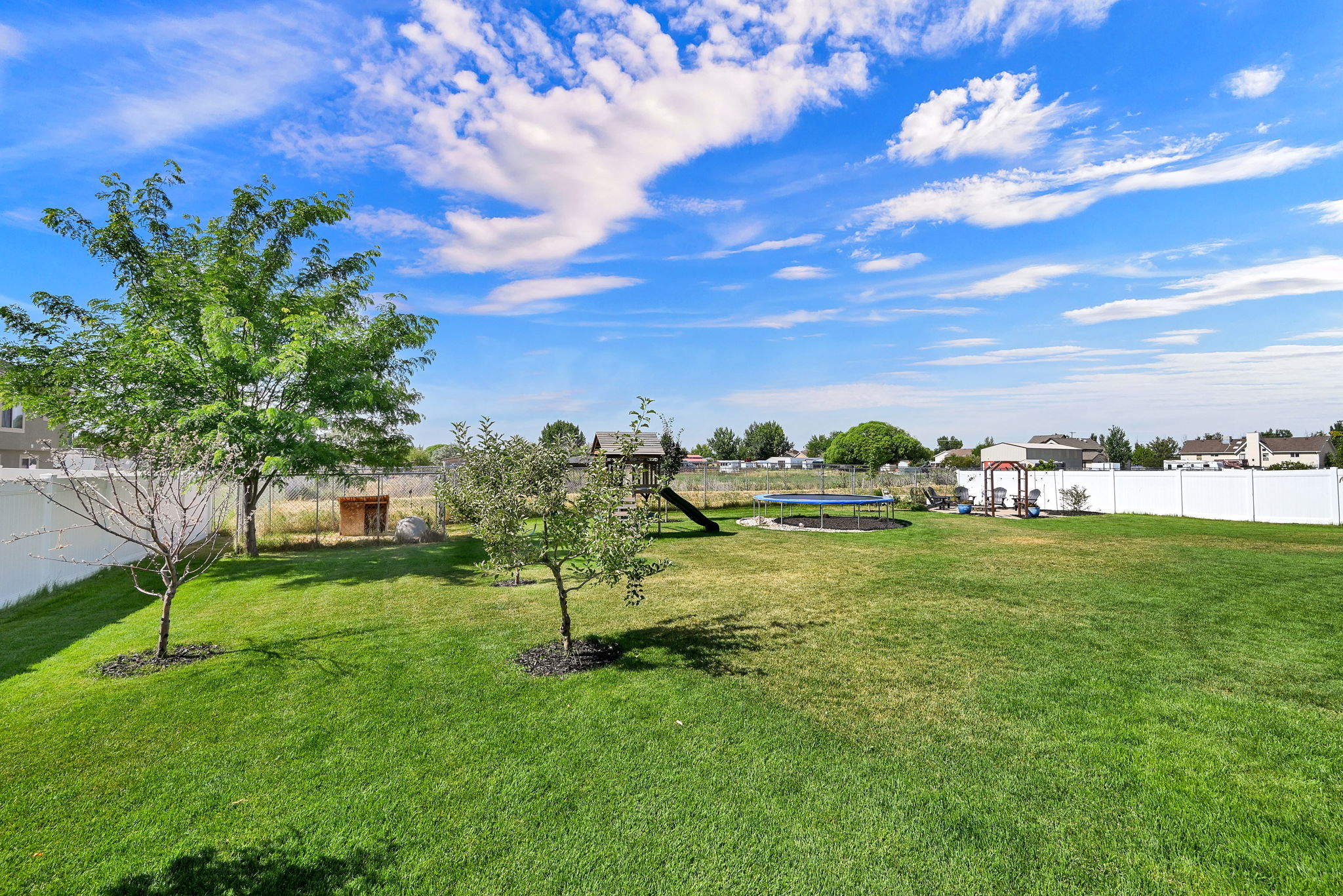 Expansive grassy yard area with mature trees and a white privacy fence