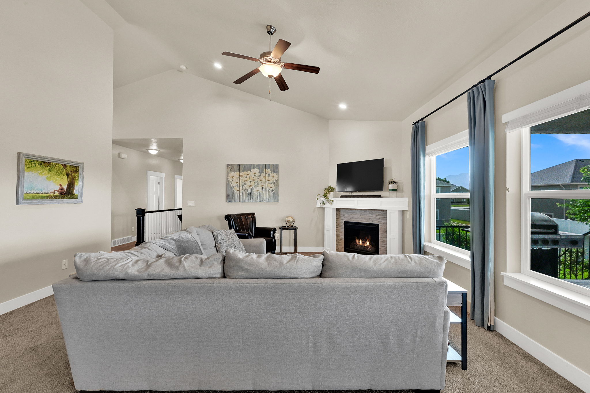 Spacious living area featuring vaulted ceilings, a ceiling fan, recessed lighting, and a gas fireplace with a stone surround and white mantle