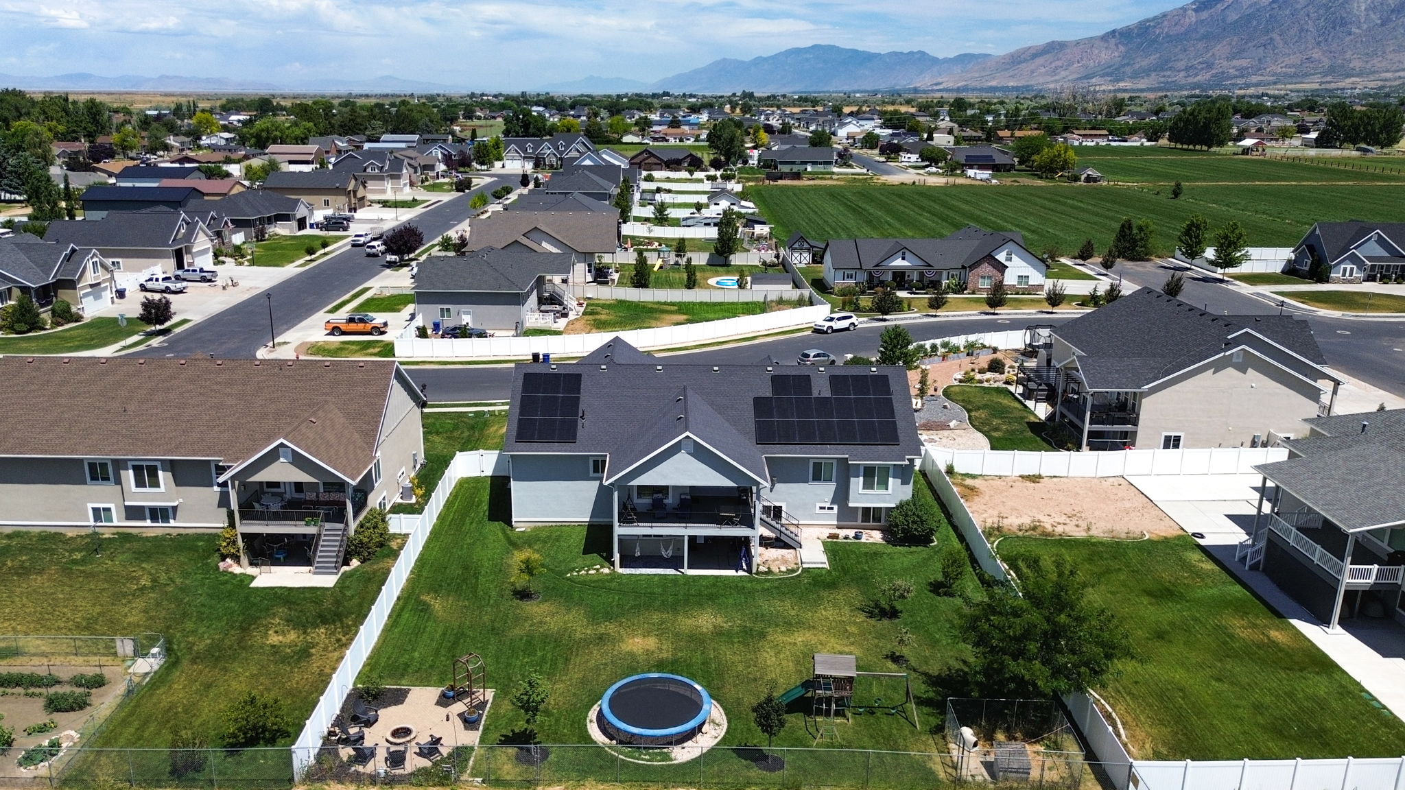 Rear exterior featuring solar panels, a tiered deck, a patio area, and a fenced backyard with green space