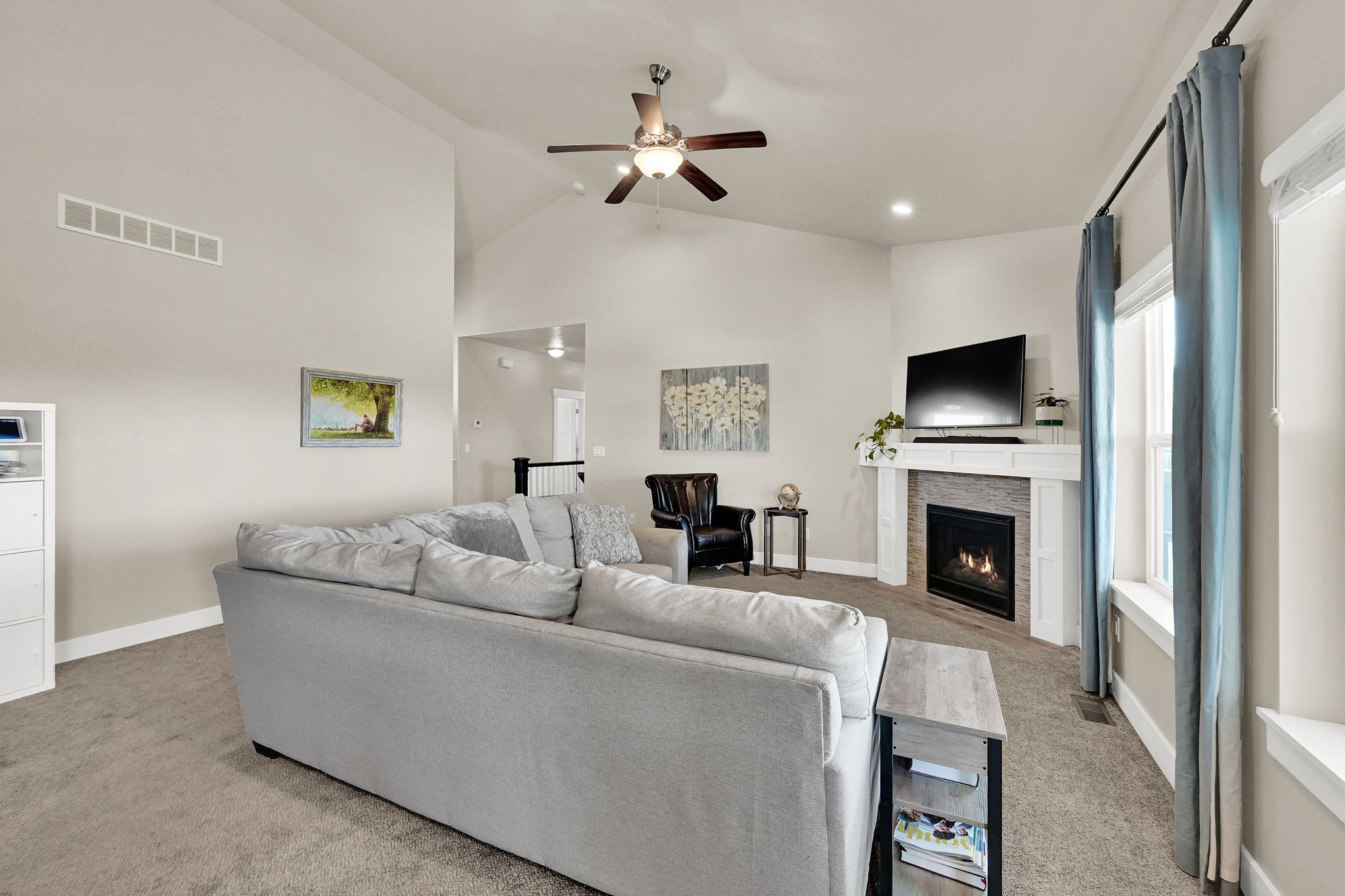 Living room featuring a vaulted ceiling with a ceiling fan, a gas fireplace with a stone surround and white mantel, recessed lighting, and a large window