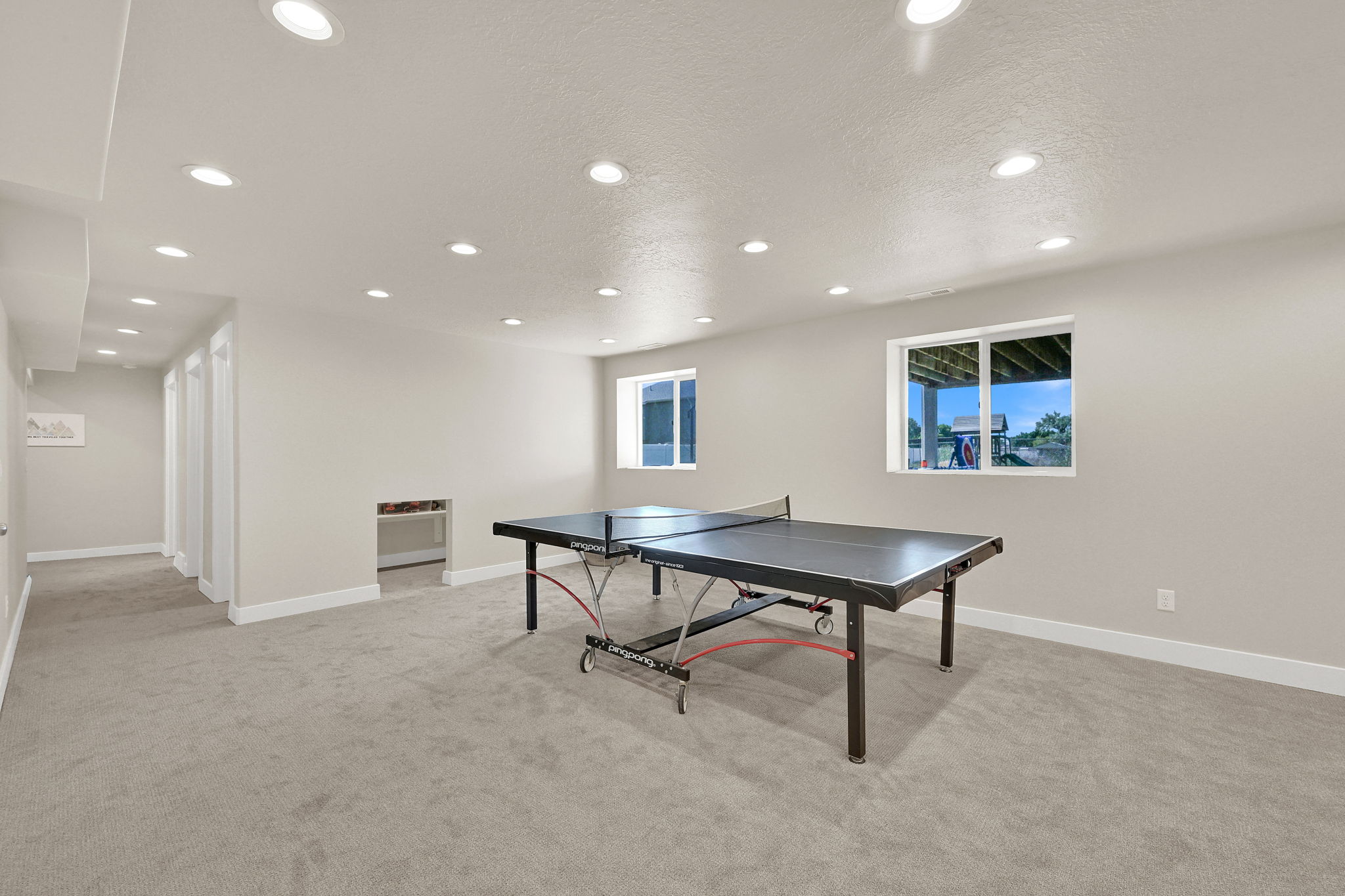 Spacious lower-level room featuring light gray carpeting, recessed ceiling lighting, and two egress windows