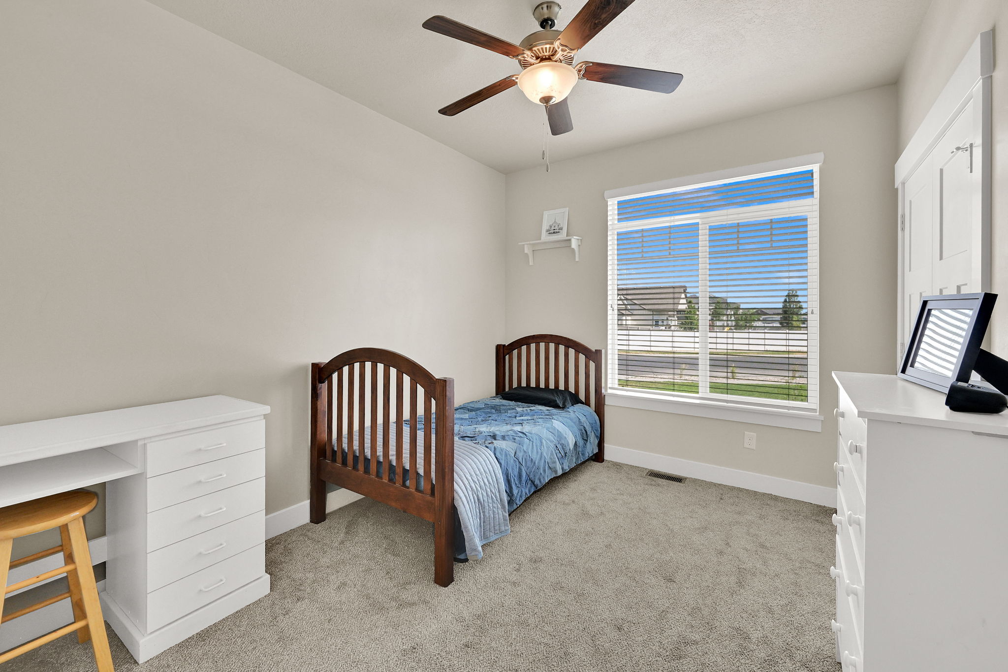 Room featuring neutral wall paint, gray carpet flooring, a large window with white blinds, and a ceiling fan with integrated lighting