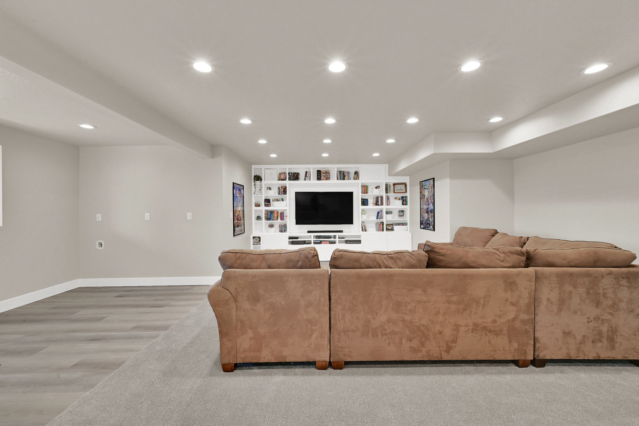 Recessed lighting illuminates this expansive space, featuring a custom built-in entertainment center with integrated shelving