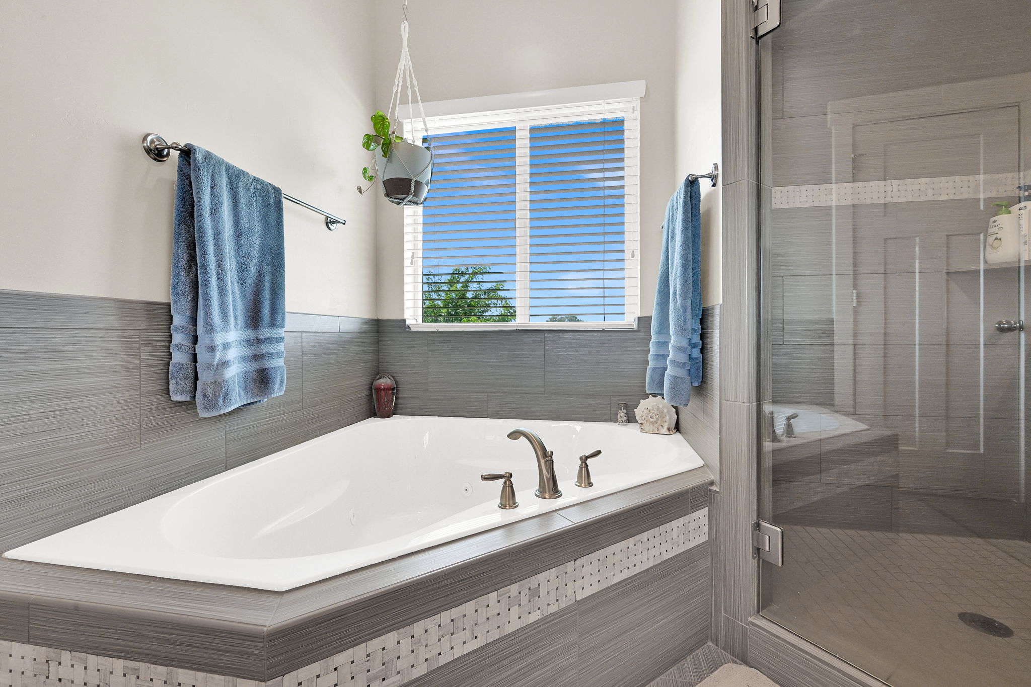 Soaking tub featuring brushed nickel fixtures and surrounding gray tile with mosaic accents