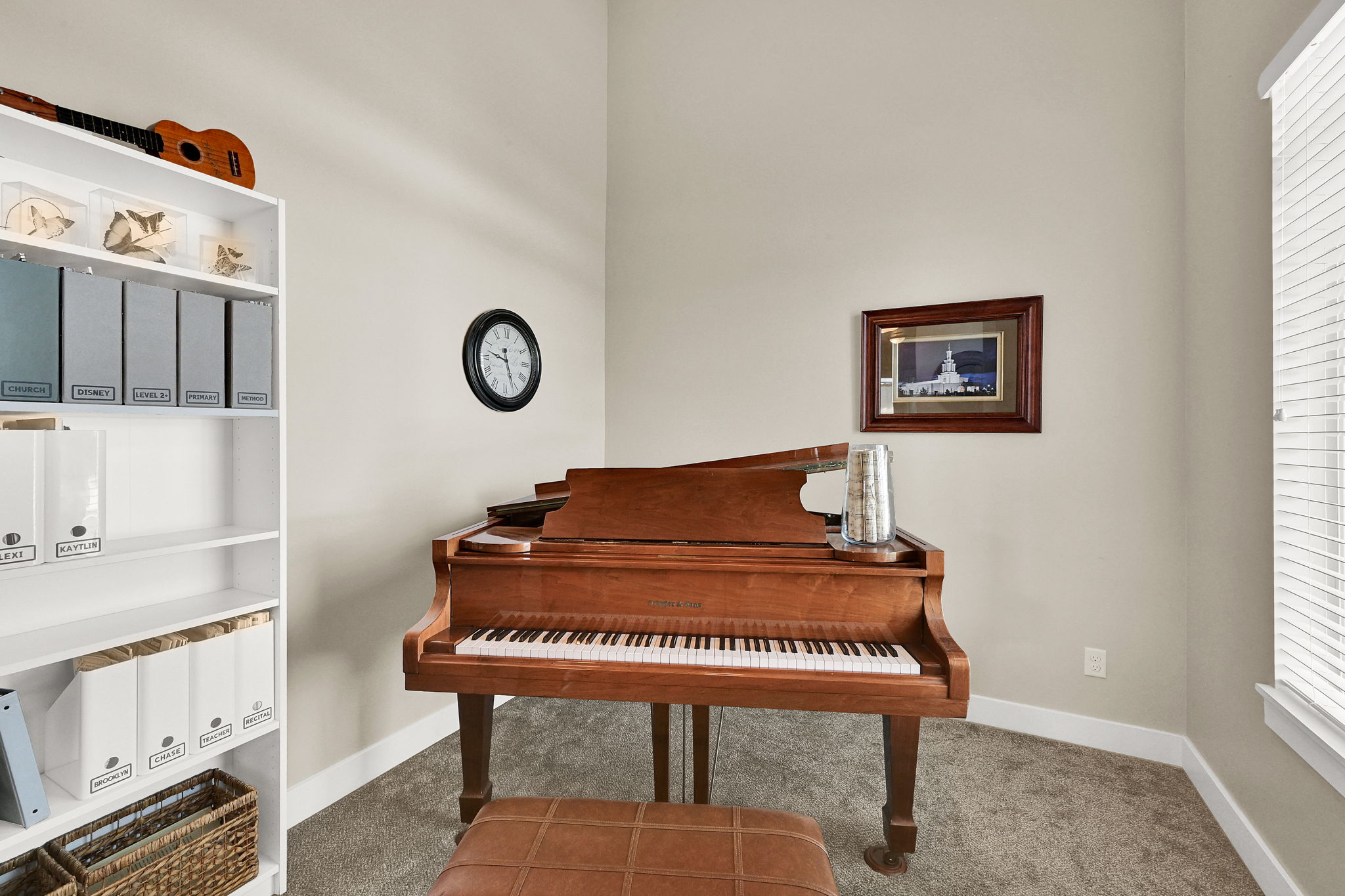 Carpeted room featuring a white built-in bookshelf, a corner window with blinds, and light neutral wall paint
