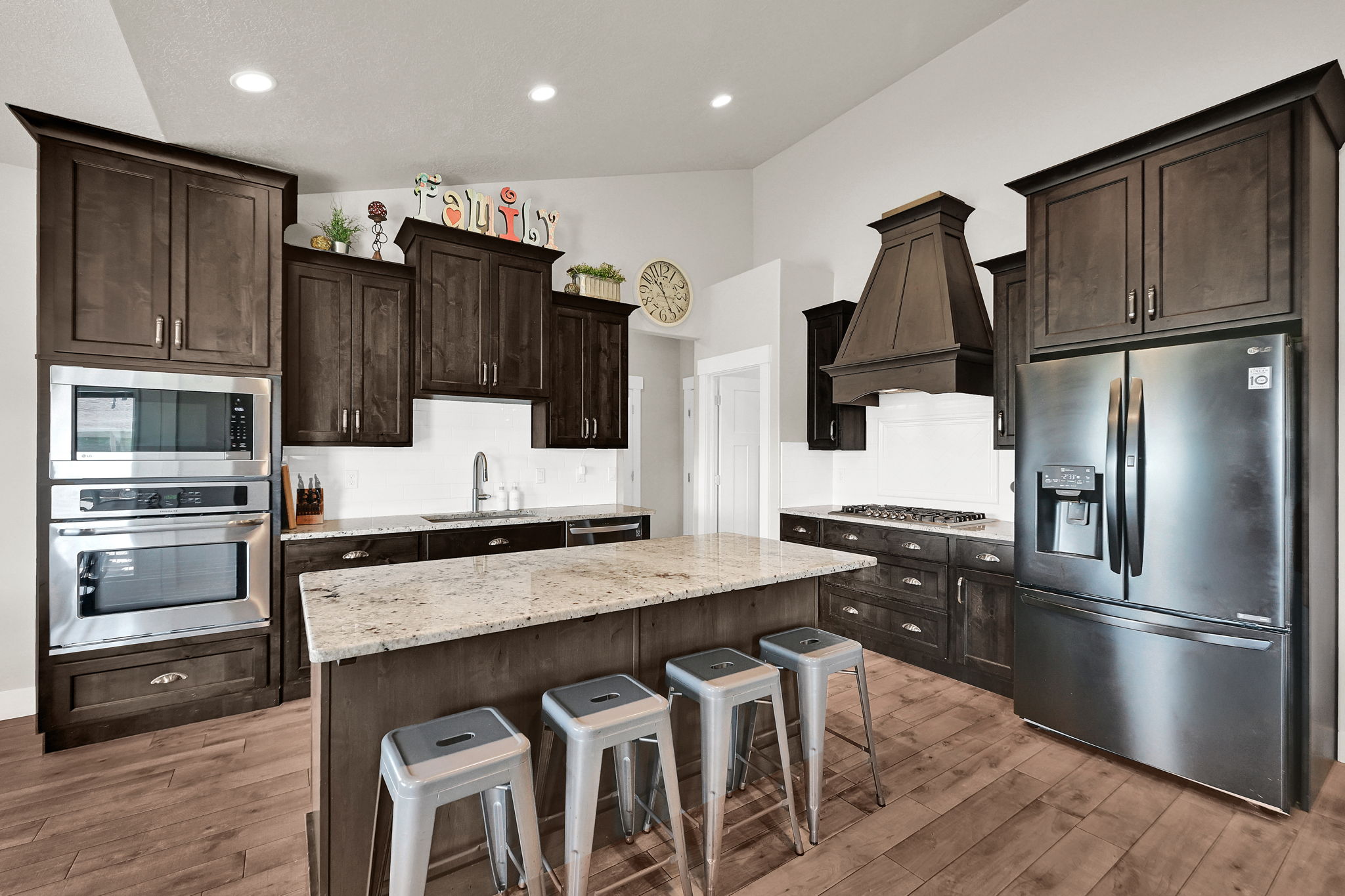 Spacious kitchen featuring dark wood cabinetry, a large center island with a light-toned countertop, stainless steel appliances, wood-finish flooring, and recessed lighting