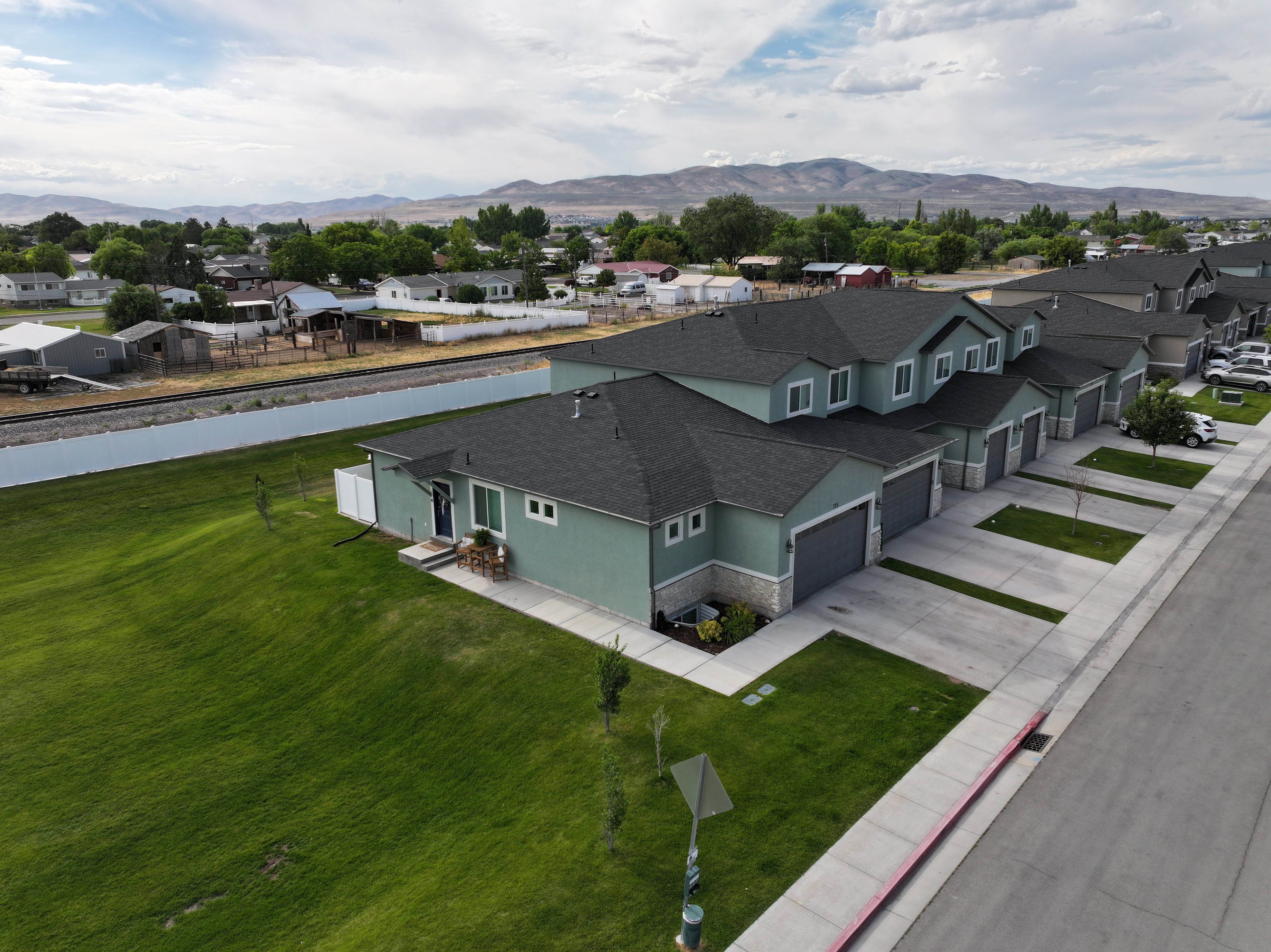 Contemporary residential structure featuring a sage green exterior with stone veneer accents, an attached two-car garage, and a charcoal shingle roof
