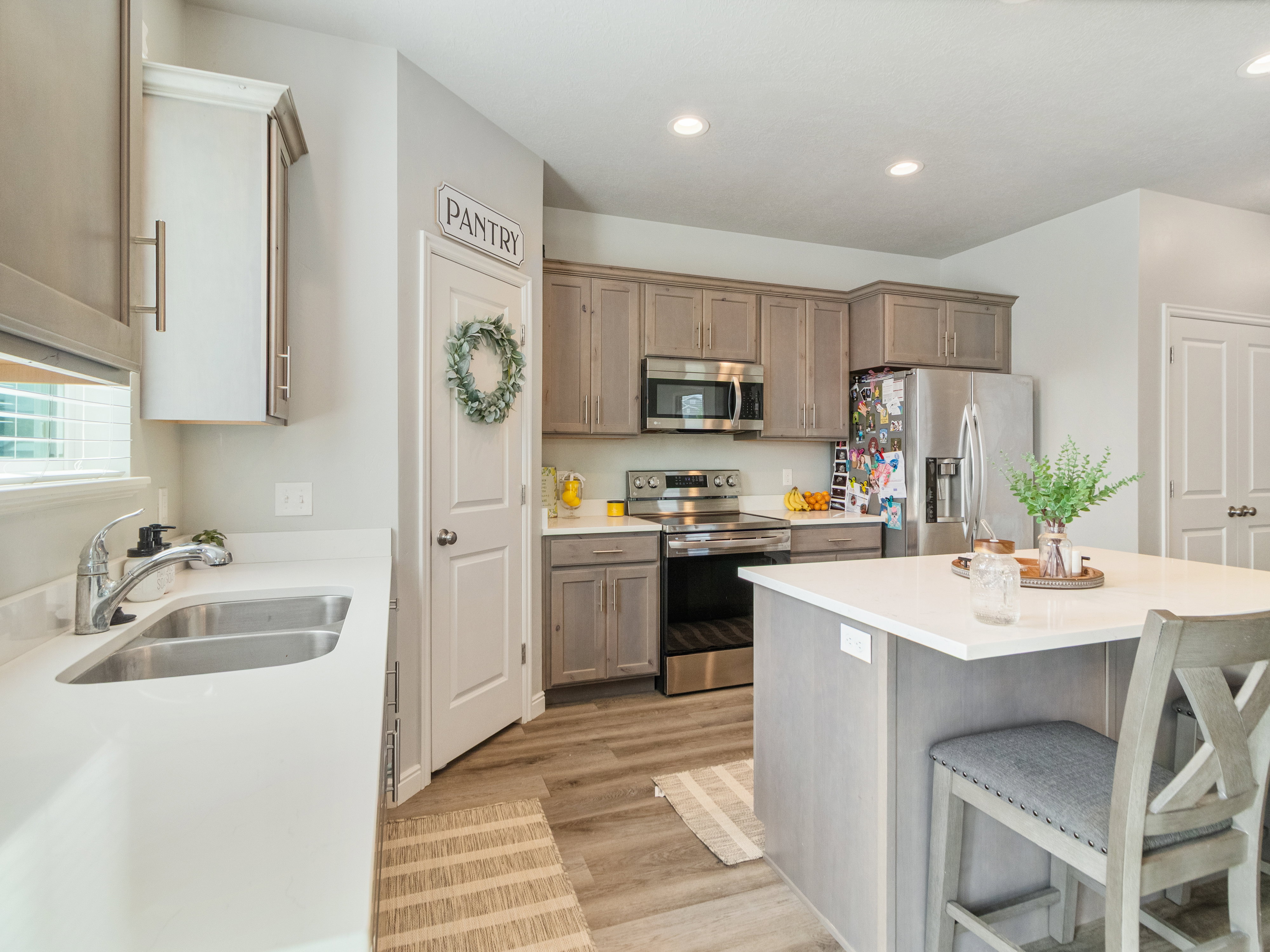 Kitchen featuring an island with seating, stainless steel appliances, light wood-finish cabinetry, a double basin sink, and wood-look flooring