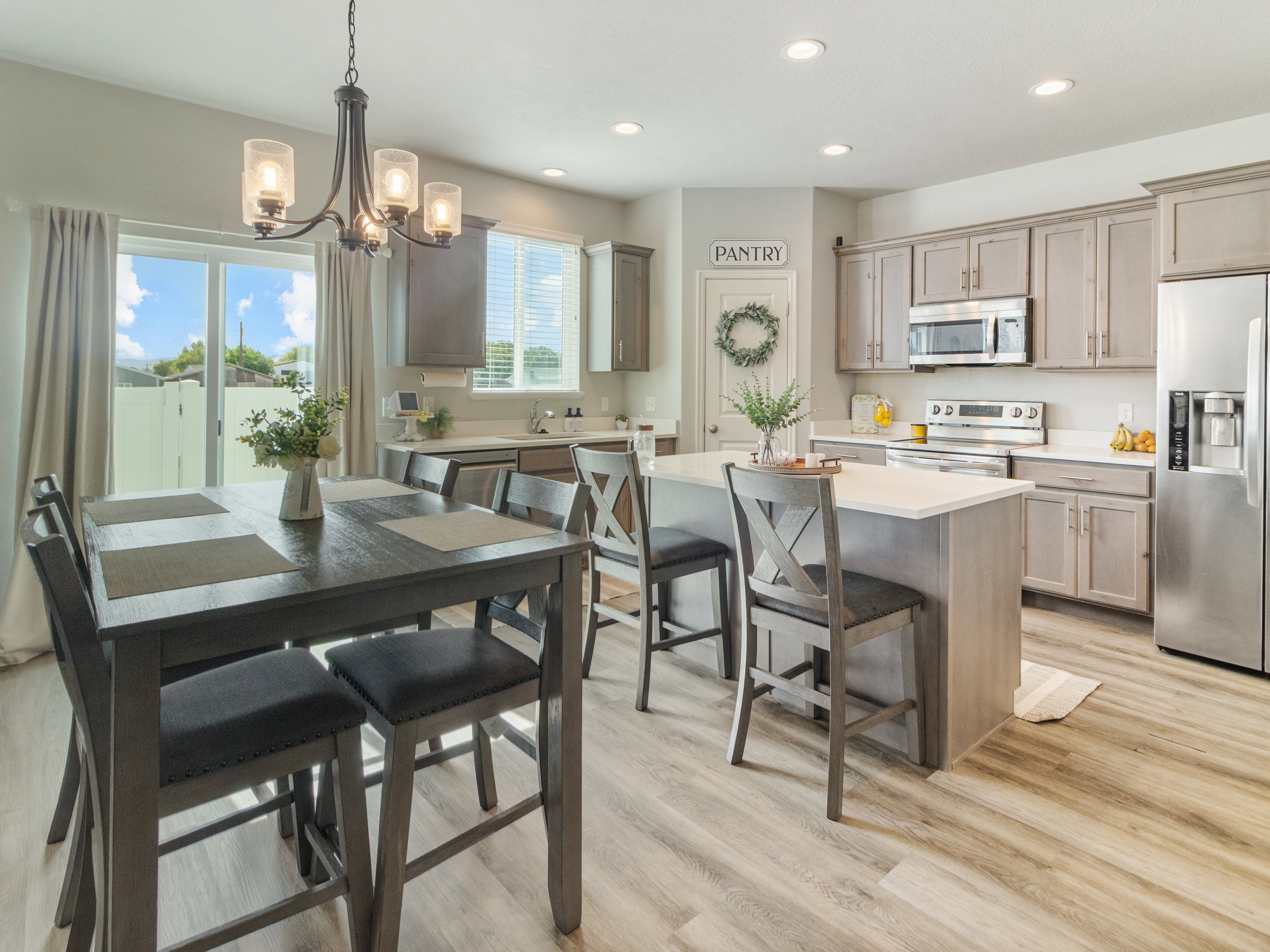 Open-concept kitchen and dining area featuring light wood-finish flooring, a central island with Quartz countertop & seating, stainless steel appliances, recessed lighting, and sliding glass doors