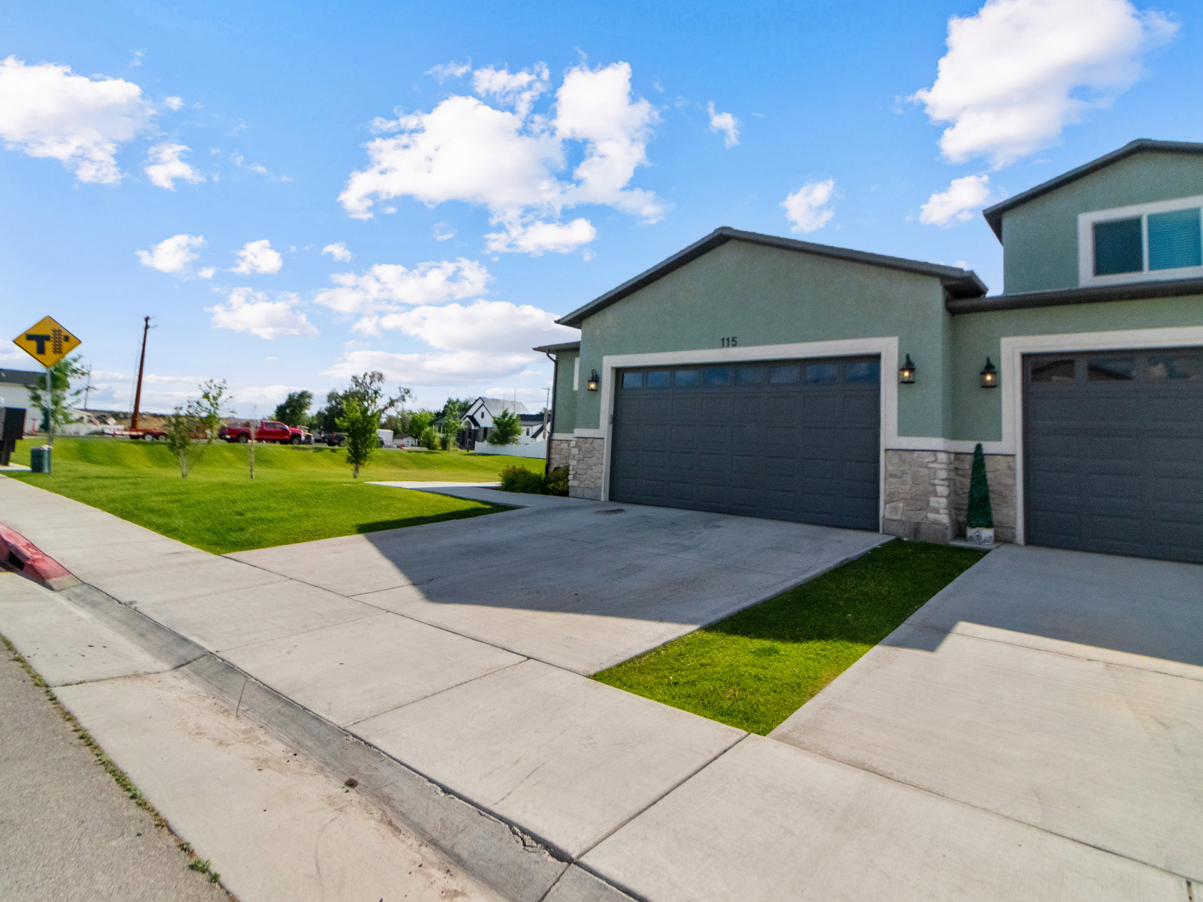 2 Car Garage. Green stucco exterior with stone accents and dark garage doors