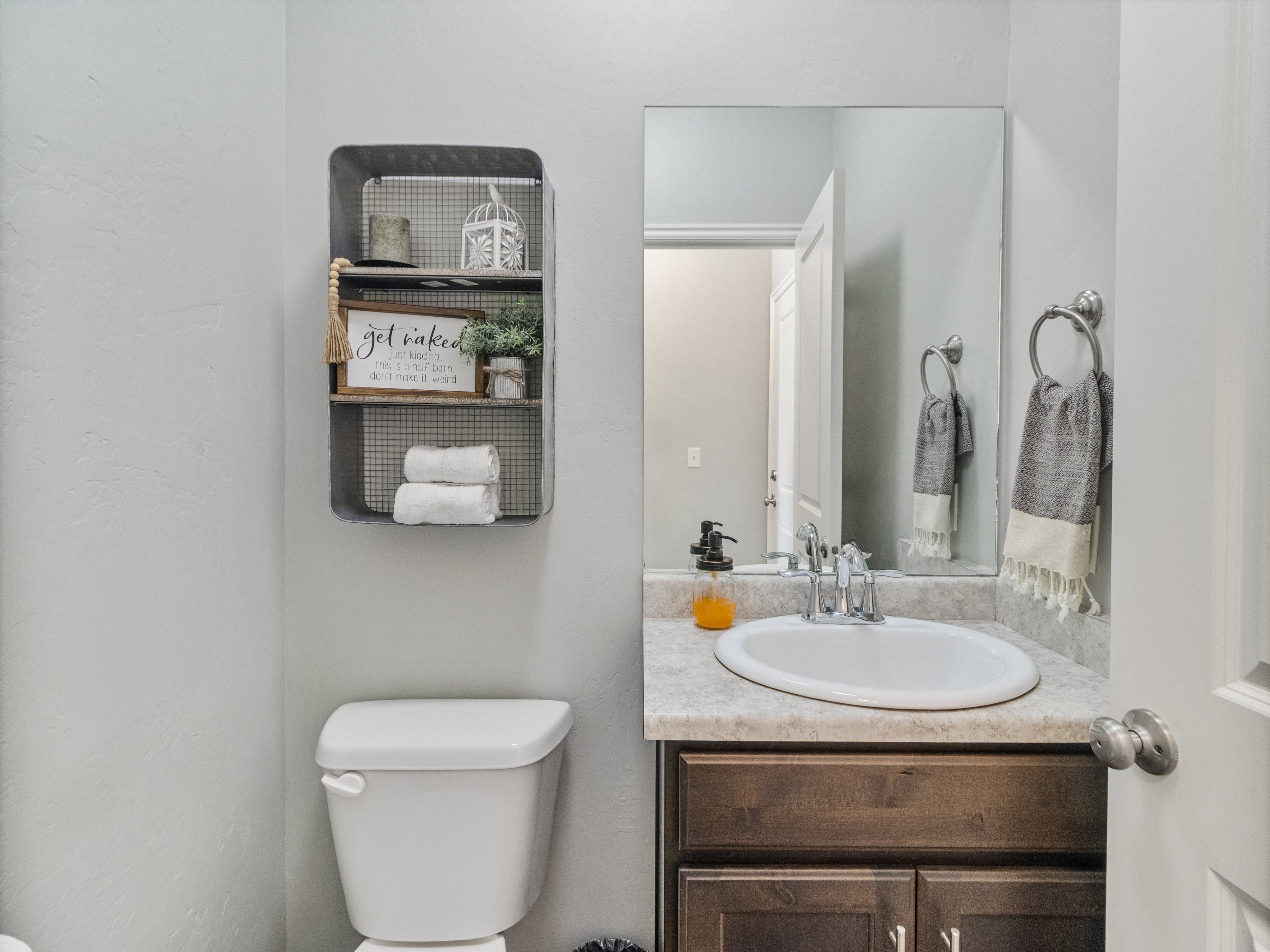 Neutral-toned bathroom featuring a white toilet, a built-in vanity with a sink, a wall-mounted mirror, and a wall-mounted storage shelf