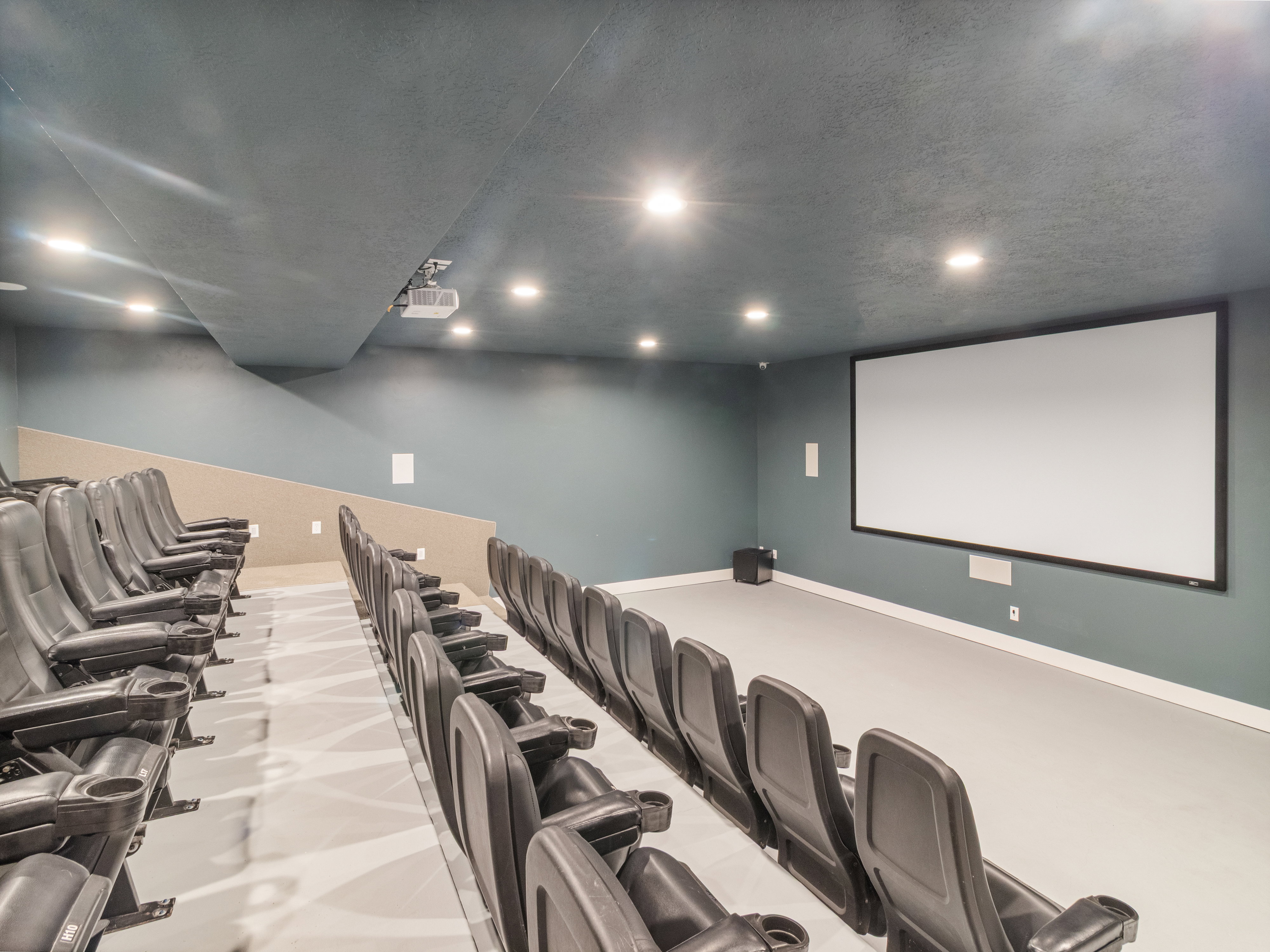 Clubhouse. Dedicated media room featuring tiered seating, a large projection screen, recessed lighting, integrated speakers, and a ceiling-mounted projector