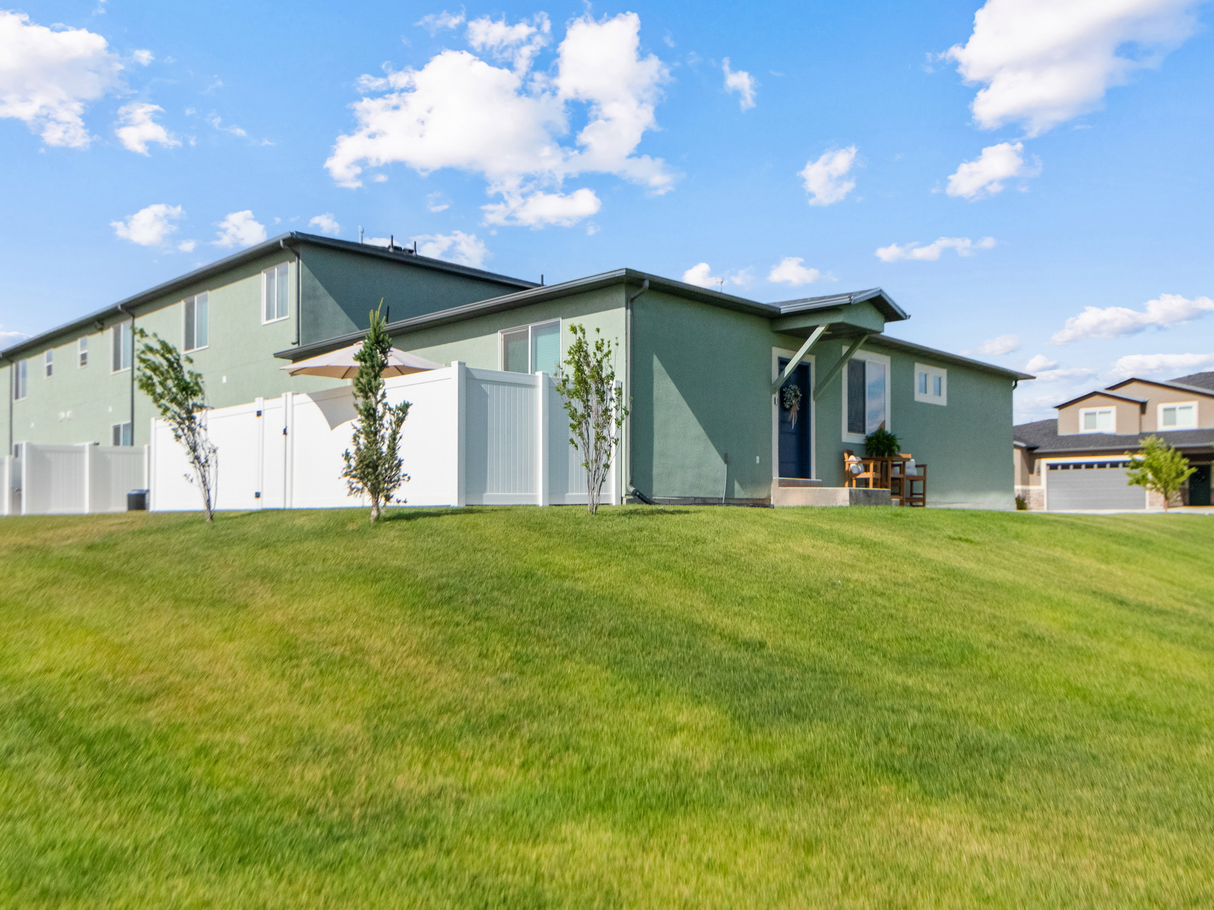 Modern residence featuring a green stucco exterior, dark entry door, and a white privacy fenced in patio. End uniit.