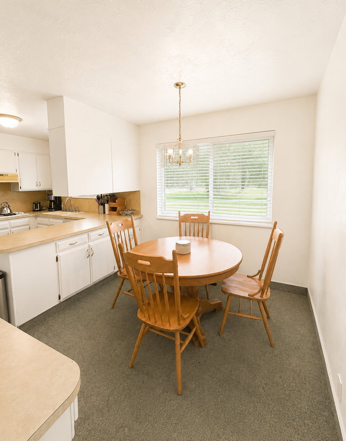 Kitchen eating area with a large window, brass chandelier, and light-colored countertops