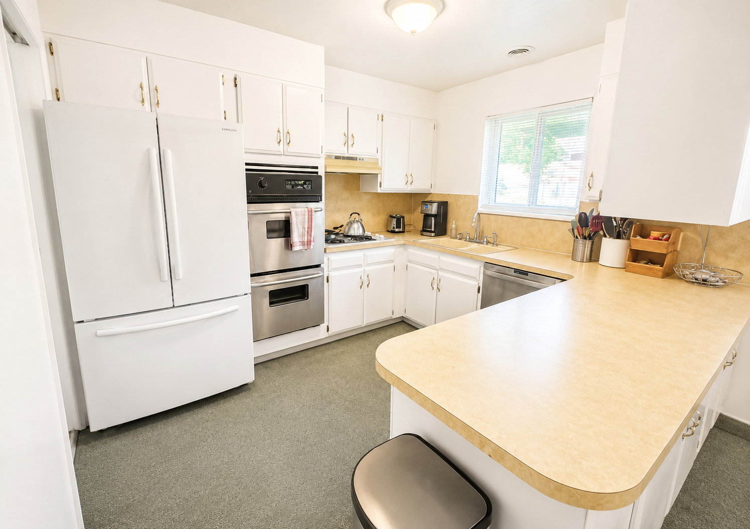 Kitchen featuring extensive white cabinetry, integrated stainless steel double ovens, a built-in cooktop, light-toned countertops, and a window above the sink