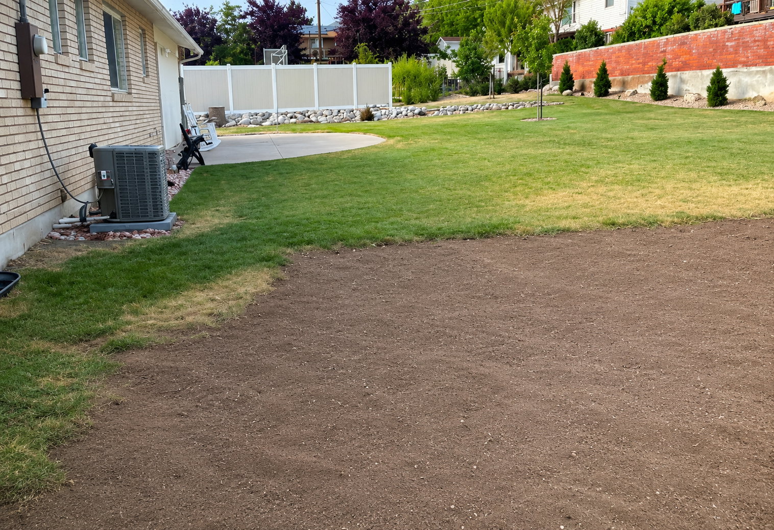Spacious outdoor area with a large prepared soil bed, an adjacent green lawn, and a curved concrete patio