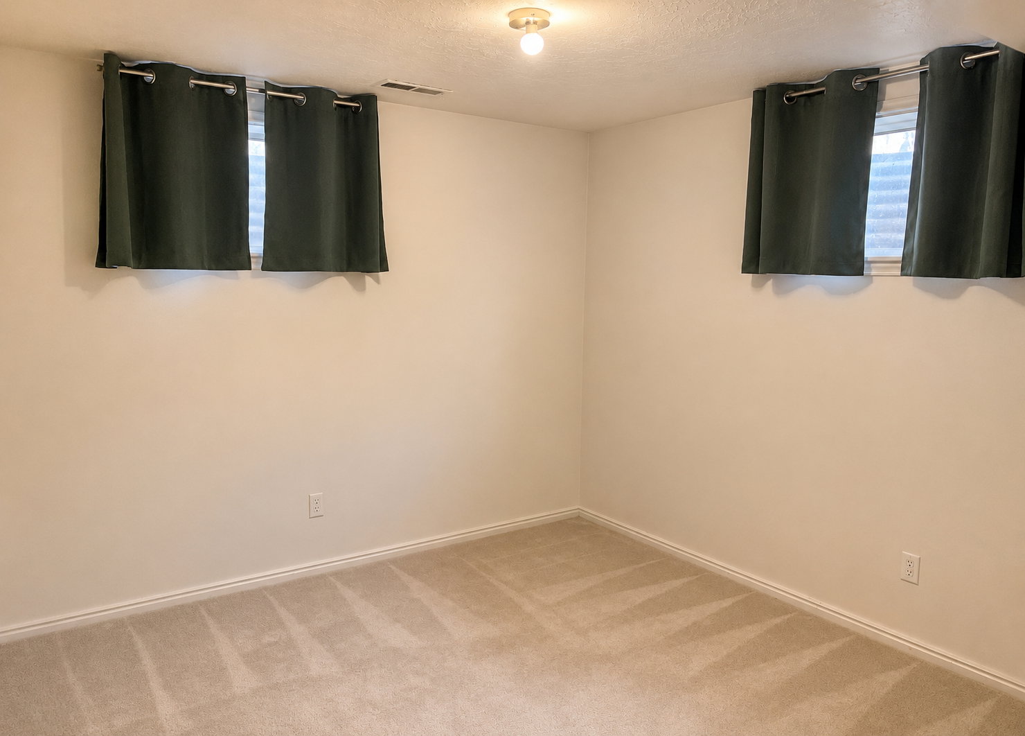 Carpeted room with neutral wall tones and two windows featuring  drapery