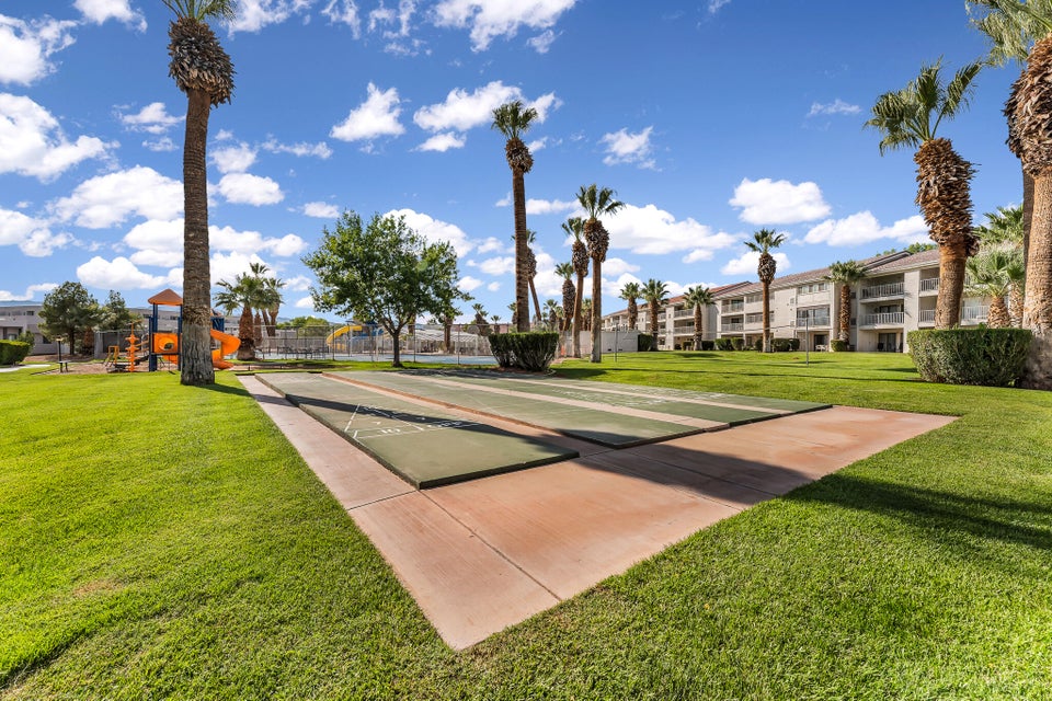 Expansive green space featuring two shuffleboard courts, mature palm trees, and a distant playground