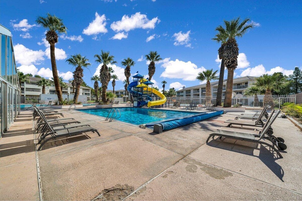 Expansive outdoor pool area featuring a large swimming pool with an attached water slide structure, surrounded by concrete decking and numerous palm trees