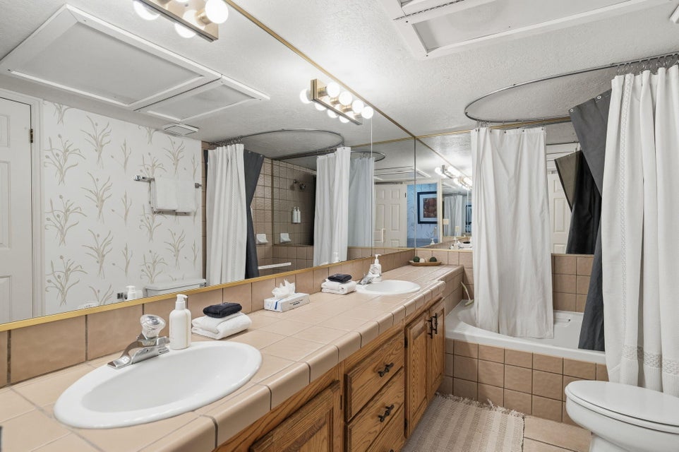 Bathroom featuring a dual vanity with integrated sinks, tile countertop, and wood-finish cabinetry