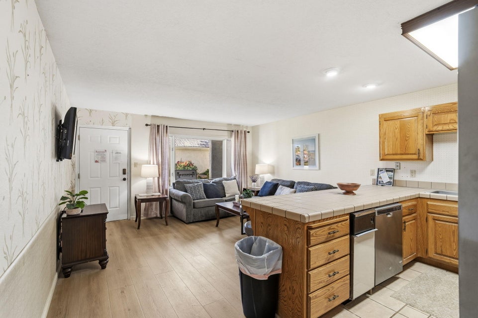 Open concept living space featuring wood-finish flooring, a kitchen peninsula with a tiled countertop, natural wood cabinetry, and a stainless steel dishwasher