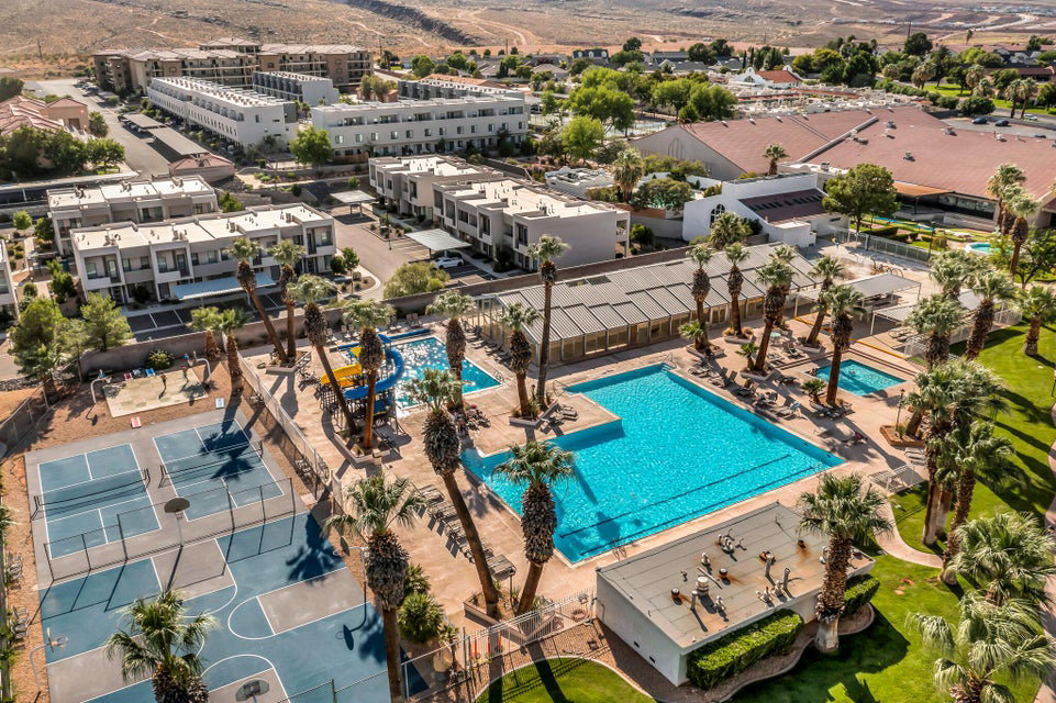 Expansive community amenity area featuring multiple swimming pools, sports courts, and mature palm trees