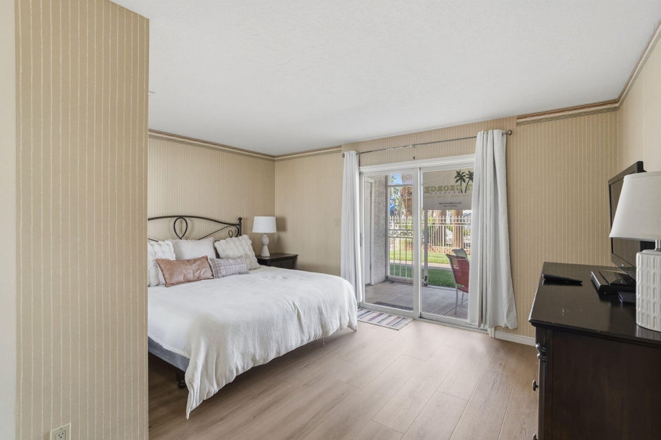 Bedroom featuring wood-finish flooring, patterned wallpaper, a sliding glass door to an outdoor patio, and a privacy wall