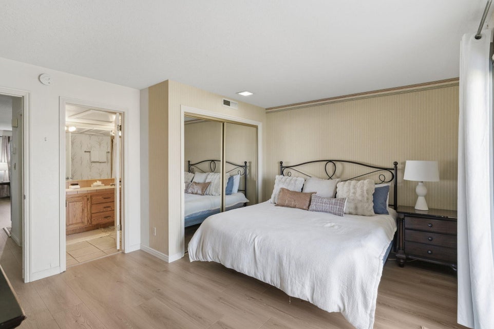 Bedroom featuring light wood-finish flooring, mirrored closet doors, and direct access to an en-suite bathroom with a vanity and wood cabinetry
