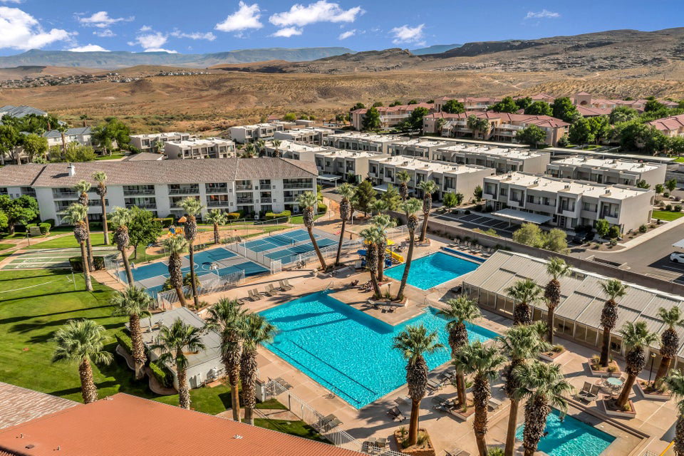 Expansive community grounds featuring a large central swimming pool, additional smaller pool, multiple tennis courts, and mature palm trees