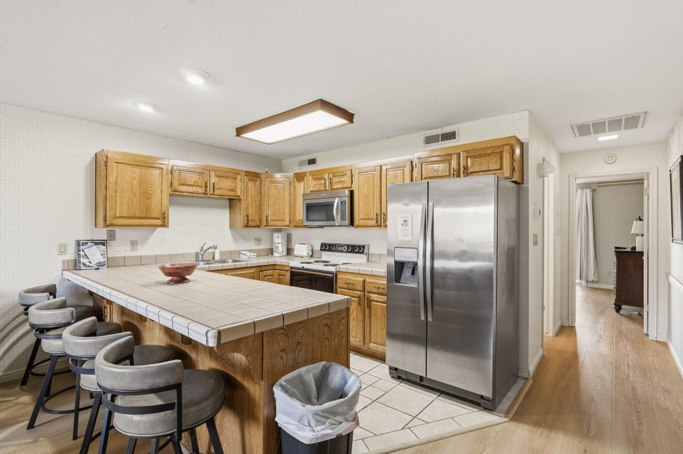 Kitchen featuring light wood cabinetry, white tiled countertops, stainless steel appliances, and an eat-at peninsula with tiled surface