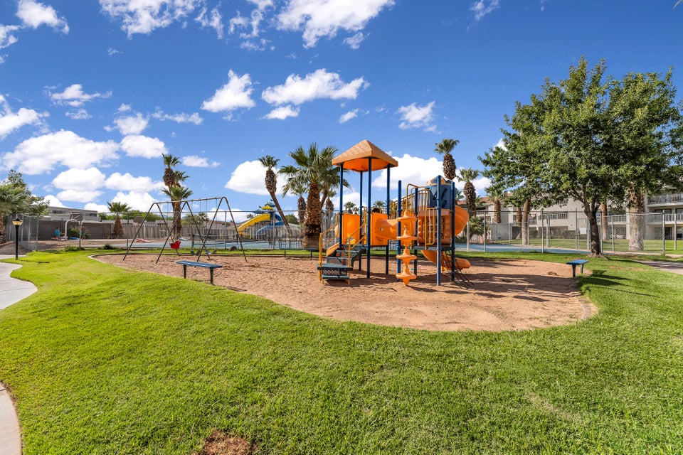 Outdoor playground area featuring a multi-level play structure with slides and climbing elements, a swing set, and a sand base