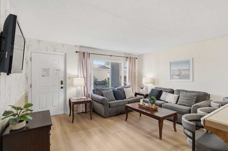 Living area featuring wood-finish flooring, a paneled entry door, and a large window with privacy curtains