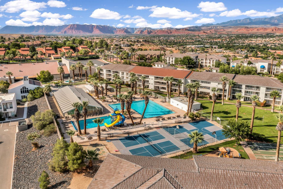 Community recreation area featuring multiple swimming pools, a covered pool structure, sports courts, and mature palm trees