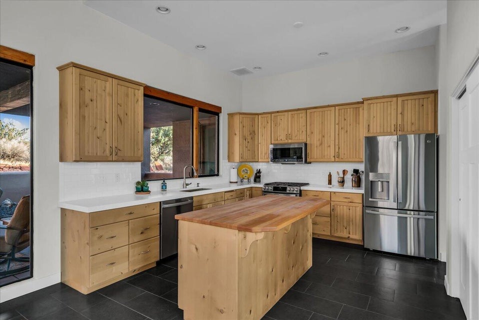 Spacious kitchen featuring natural wood cabinetry, white countertops, a subway tile backsplash, a center island with a wood countertop, and stainless steel appliances