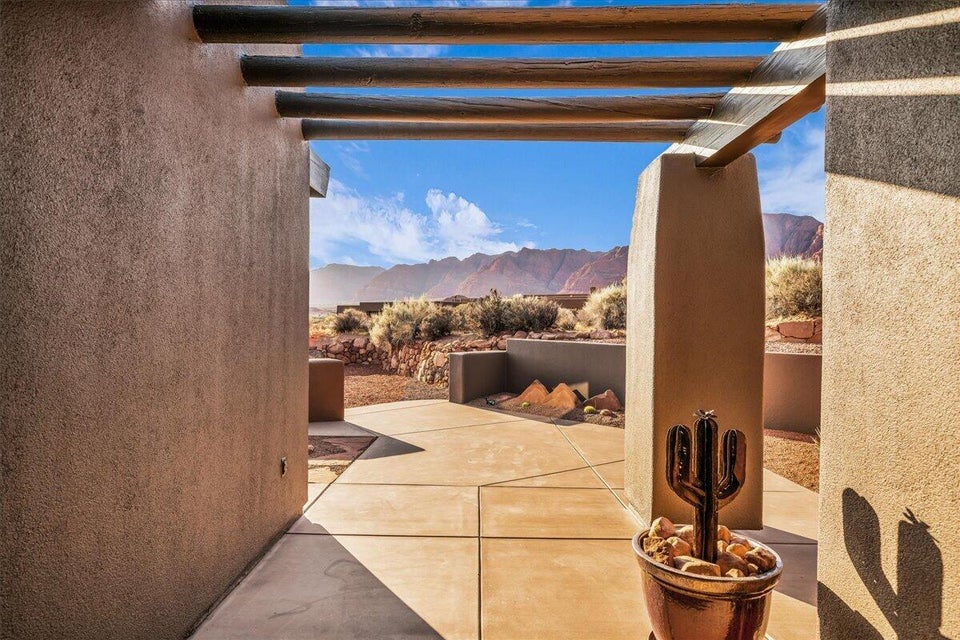 Stucco exterior with exposed wood beams, concrete patio, and desert landscaping