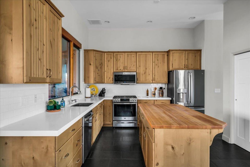 Kitchen featuring extensive light wood cabinetry, white countertops, black tile flooring, and stainless steel appliances