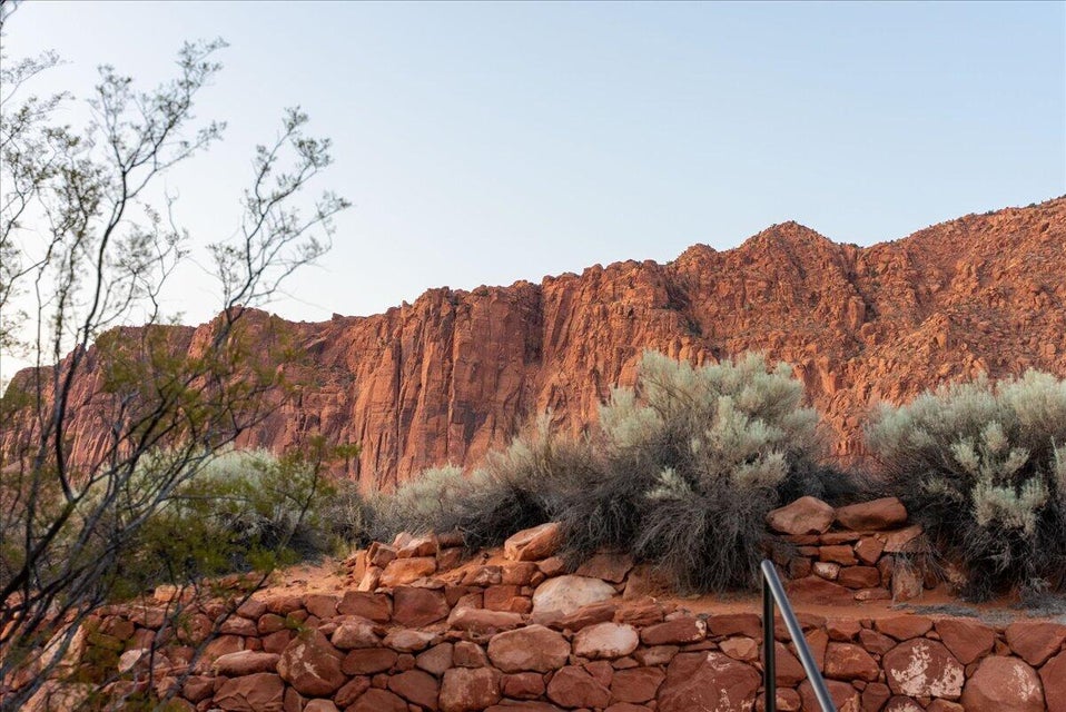 Red rock landscape featuring natural stone formations, desert scrub, and a stone retaining wall