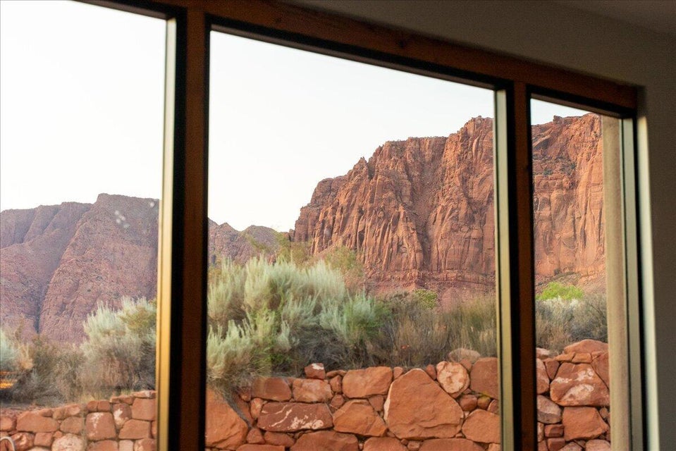 Panoramic windows framed in wood, showcasing desert landscaping with a stone wall and distant red rock mountains