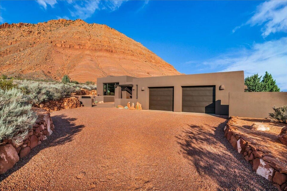 Desert modern architecture with a stucco exterior, integrated two-car garage, and stone-lined gravel driveway