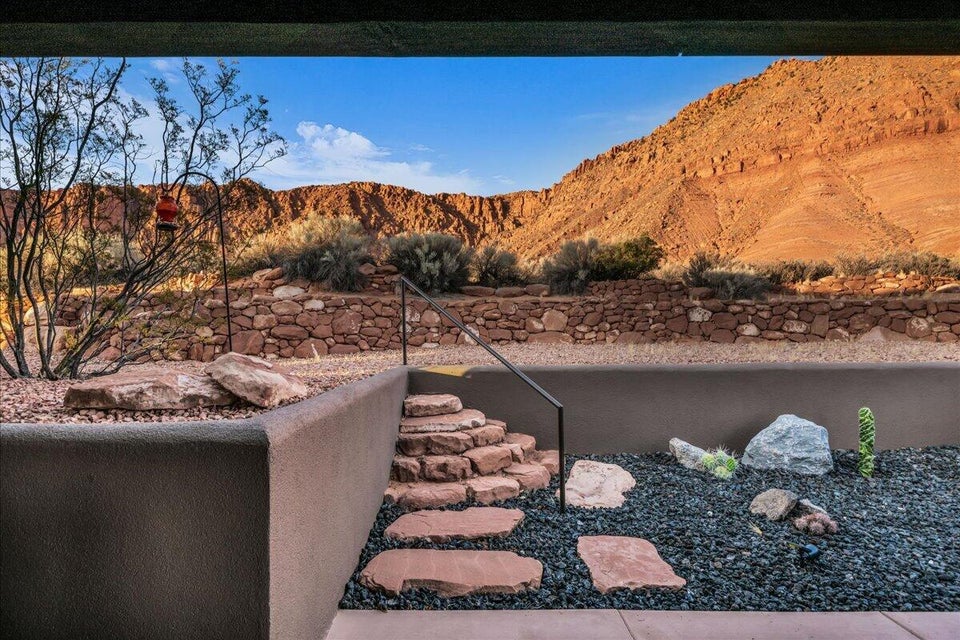Desert landscaping featuring a stone retaining wall, natural rock steps, black pebble ground cover, and native plantings