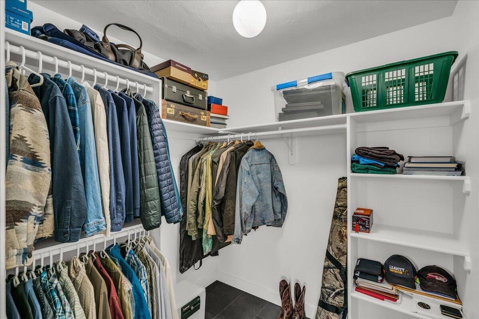 Spacious walk-in closet featuring white built-in shelving, multiple hanging rods, and dark tile flooring