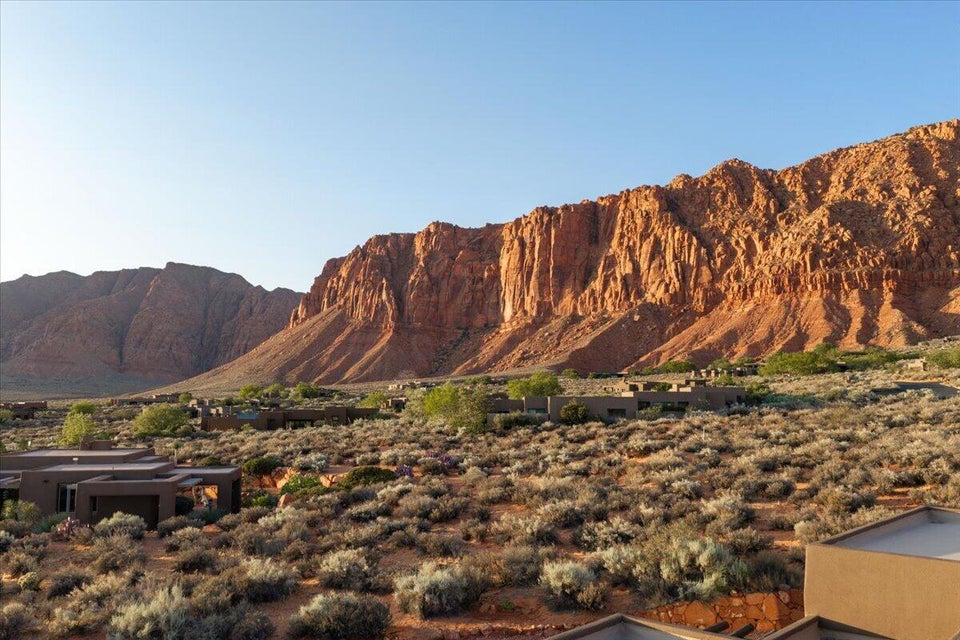 Dramatic red rock mountains frame the expansive desert landscape, featuring multiple low-profile, earth-toned structures integrated into the terrain