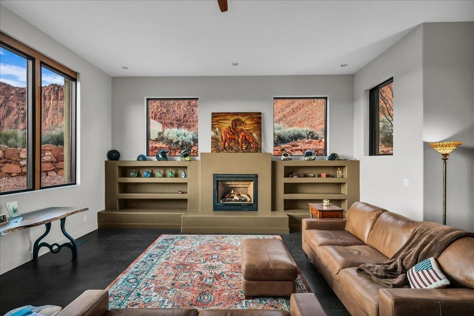 Living area featuring dark floor tile, a central fireplace with built-in shelving, recessed lighting, and multiple windows with views of red rock formations