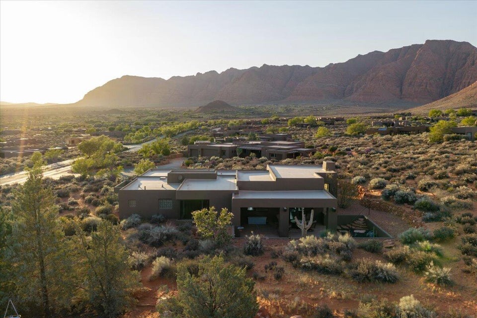 Desert landscape featuring a modern residence with flat rooflines, a covered outdoor living area, and surrounding natural vegetation